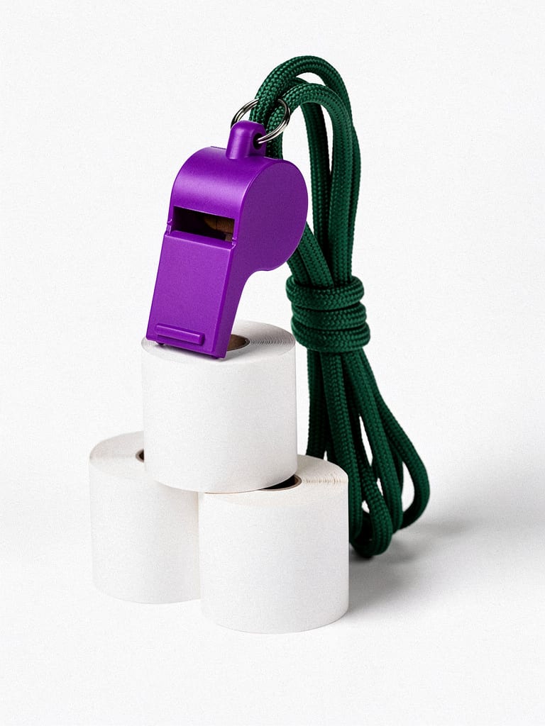 A violet coach's whistle on a green lanyard beside blank rolls of ticket paper, isolated on white.